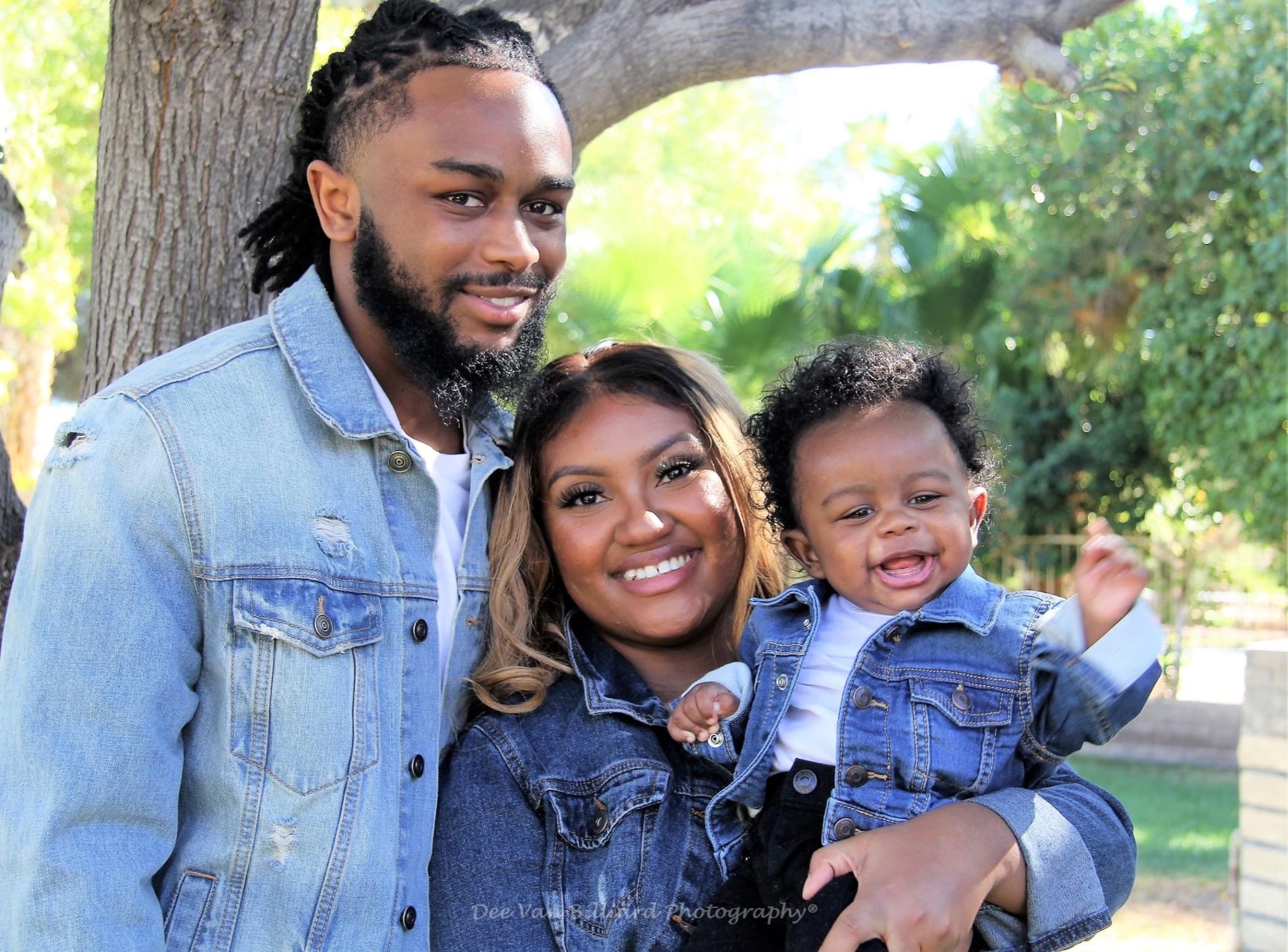 A family of three smiling beneath a tree.