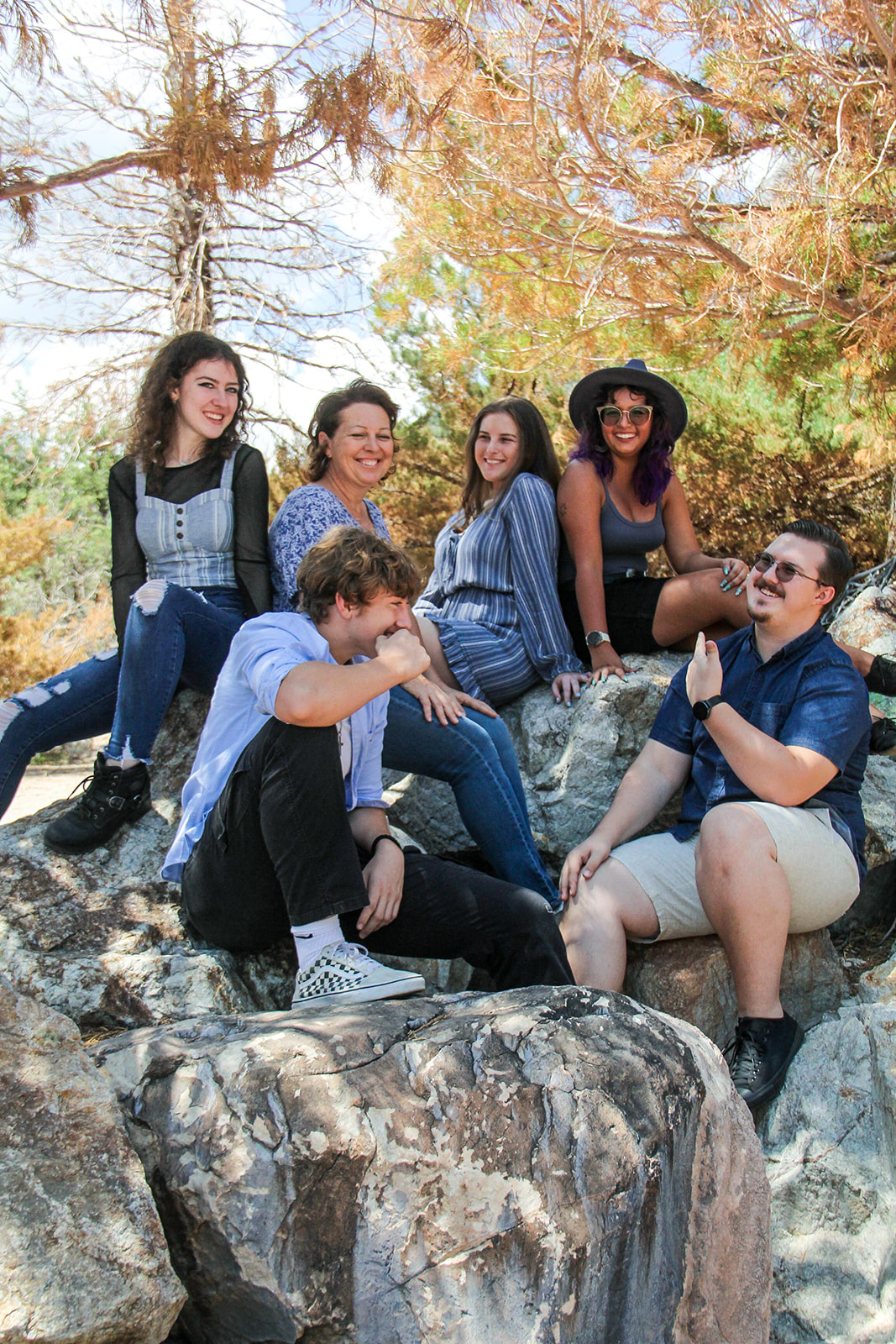 Four women and two men sit atop some boulders and pose for a photo.