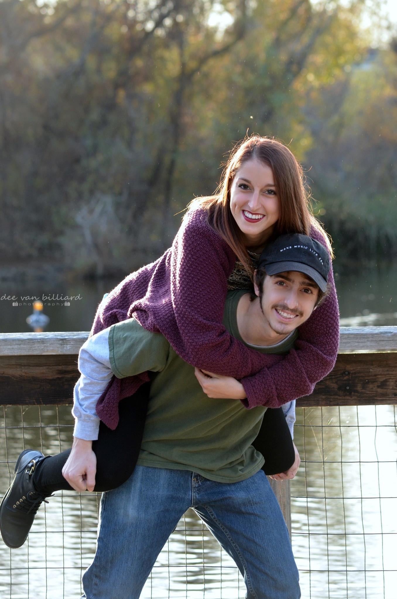 A brother carries his sister on his back in front of a lake.