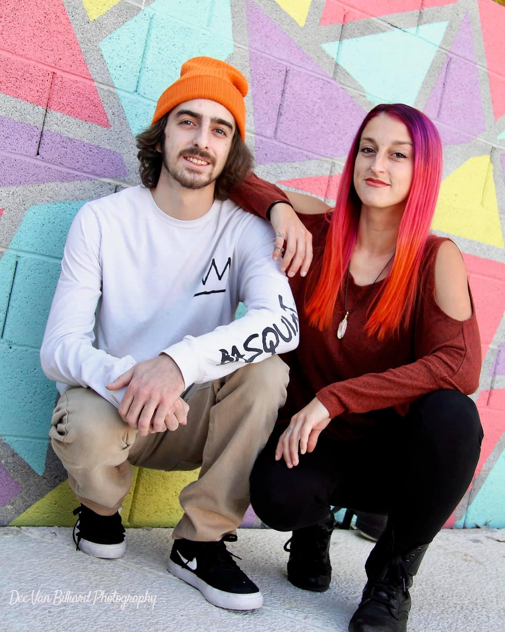 A brother and sister kneel in front of a colorful wall for a thug like photo.