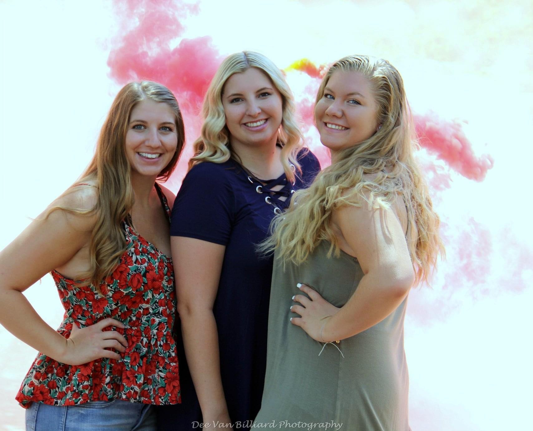 A family of three women posing in front of some colorful smoke.