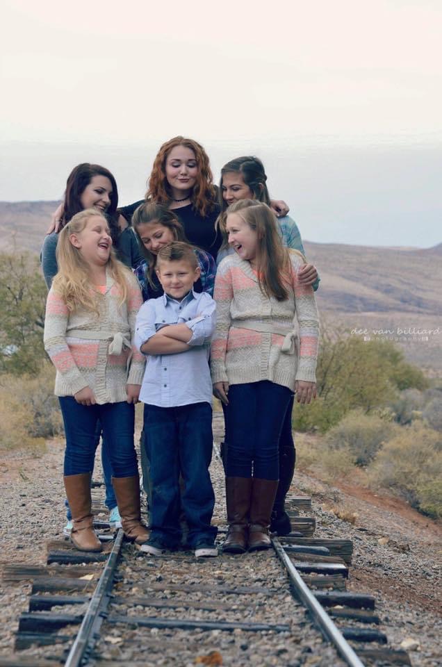 A mother with 6 of her kids pose on top of a railroad track.