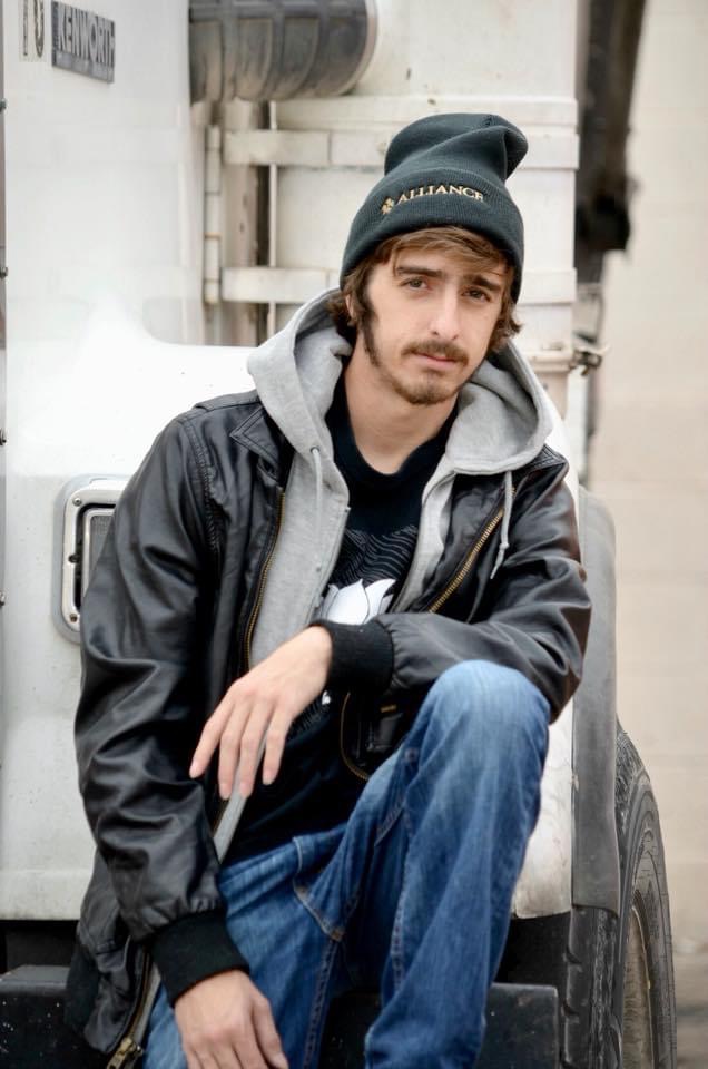 A young rapper poses for a photo in front of a truck.