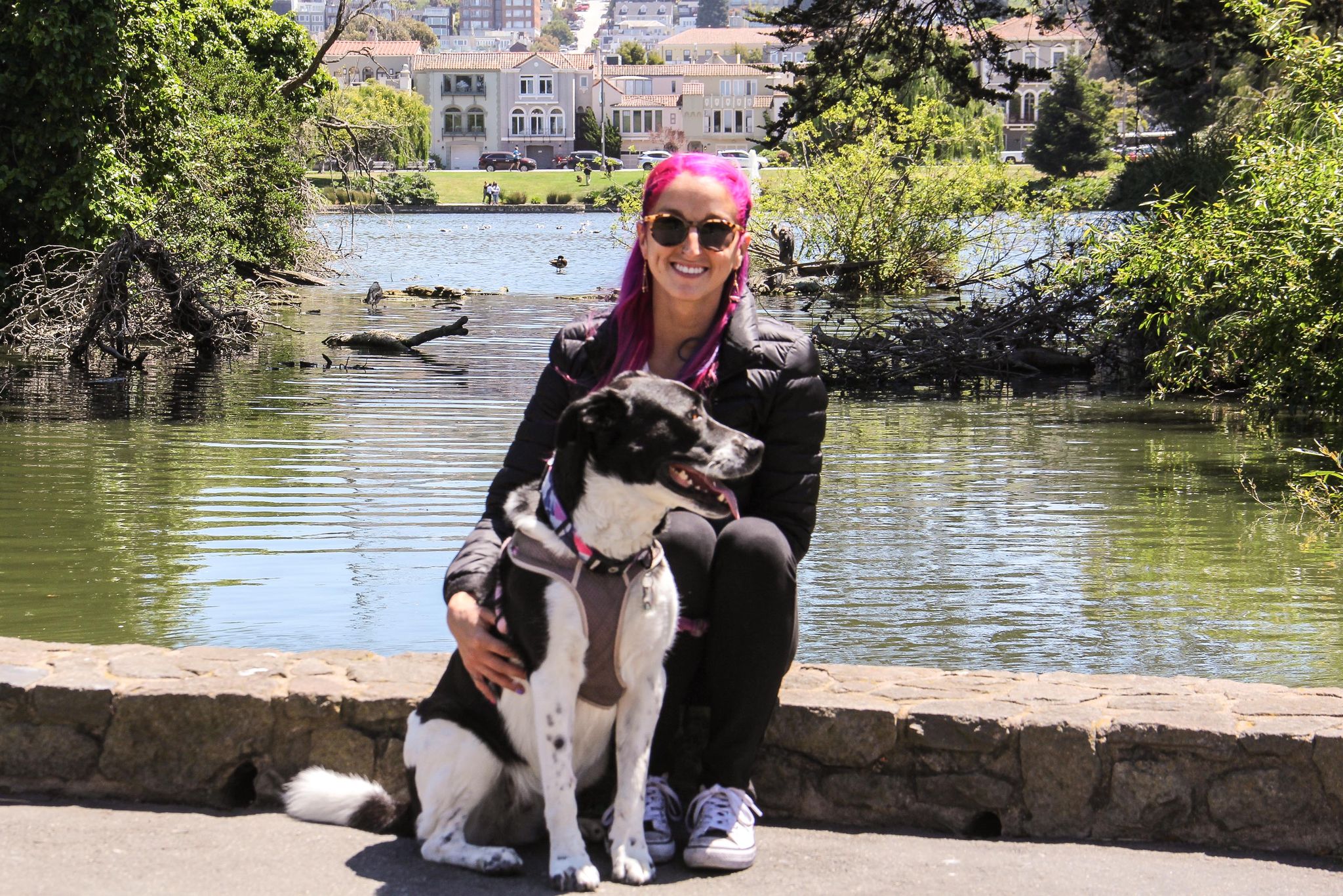 A woman and her black and white dog pose in front of a small body of water.