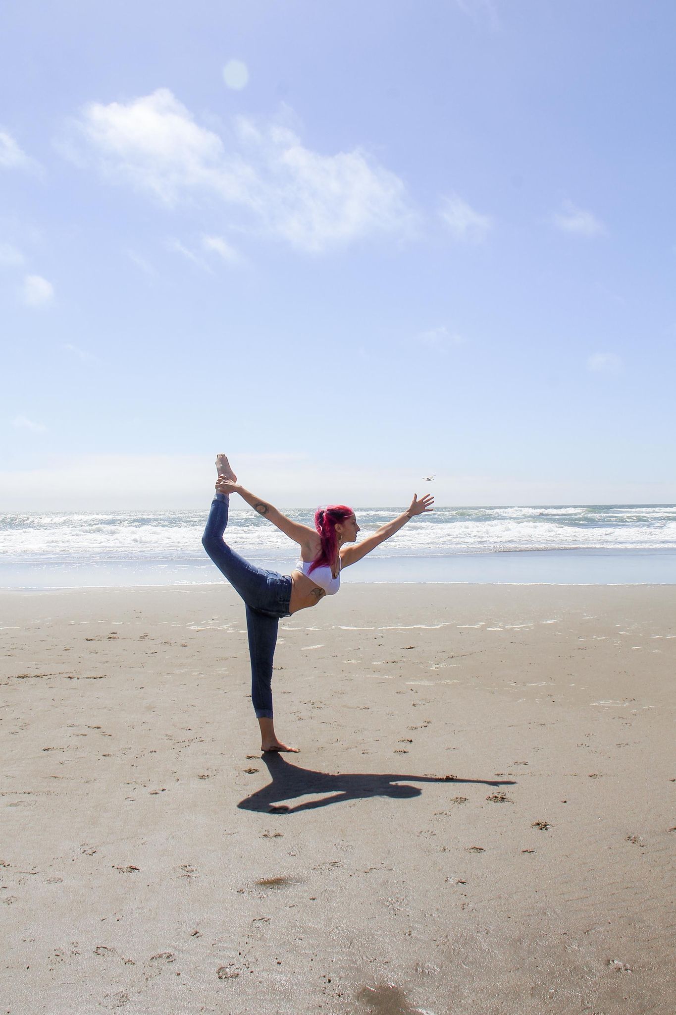 A beautiful woman with colorful hair balances on top of one leg at the beach.