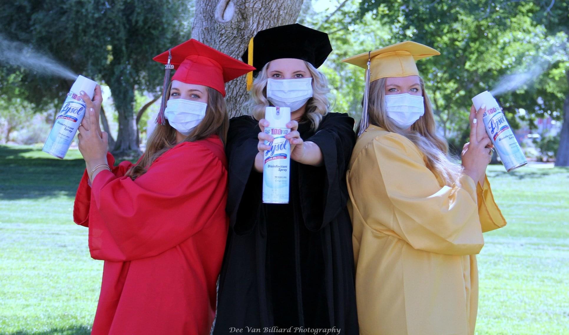 Three women in caps and gowns wearing medical masks pose for the camera with cans of Lysol.