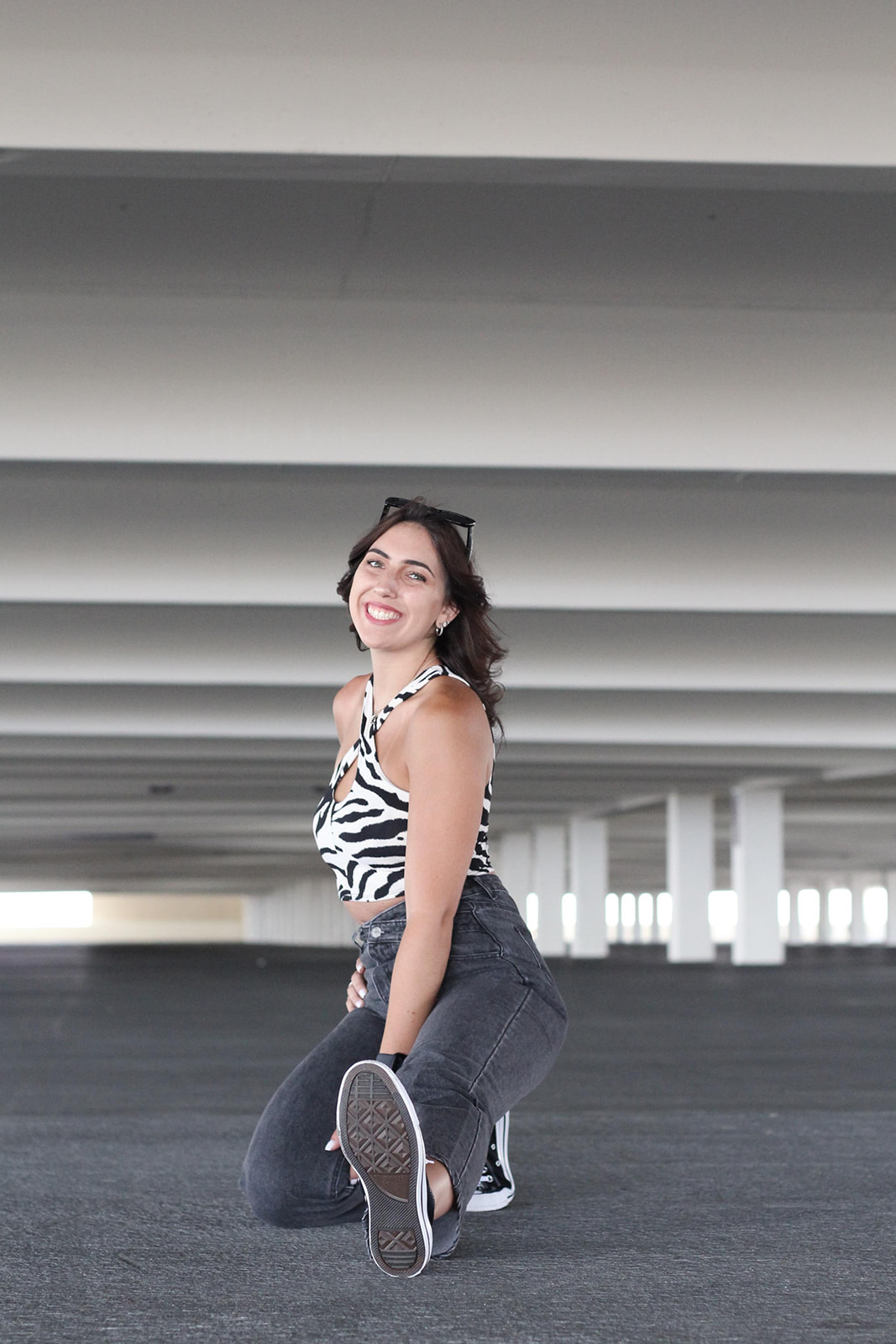 A young lady kneeling with a leg out poses in a parking garage.