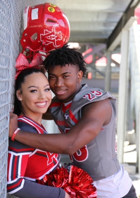 A young cheerleader and football player pose beneath the bleachers.