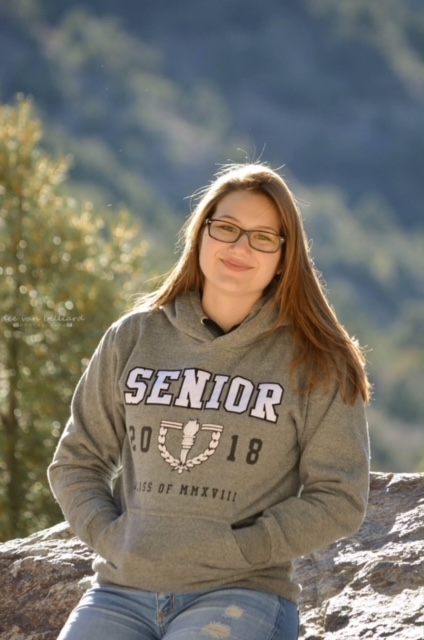 A young lady smiles for a photo while sitting outside against a boulder.