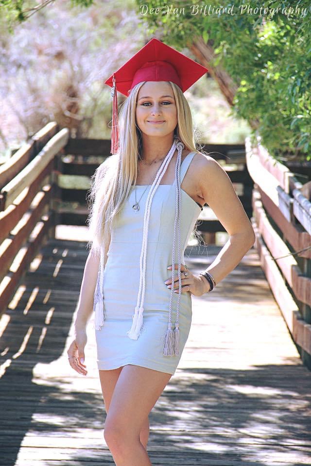 A young lady wearing a graduate's cap poses on a bridge.