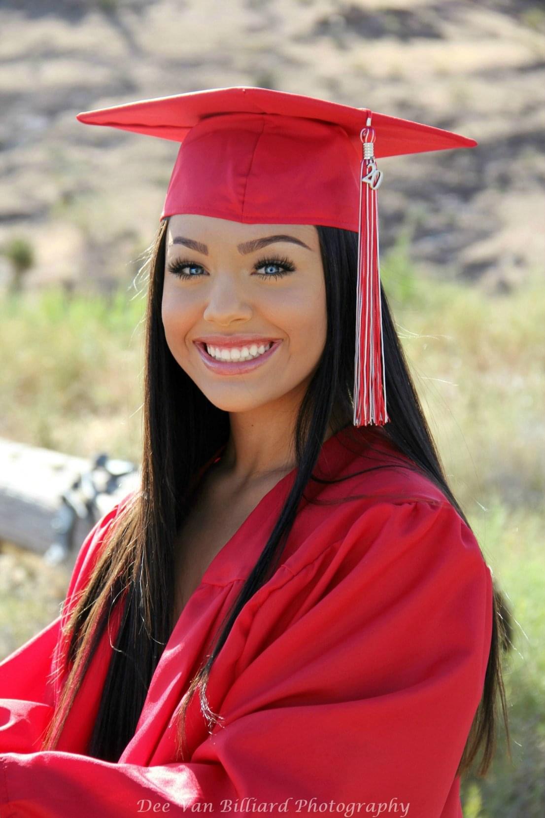 A young lady smiling outside in her cap and gown.