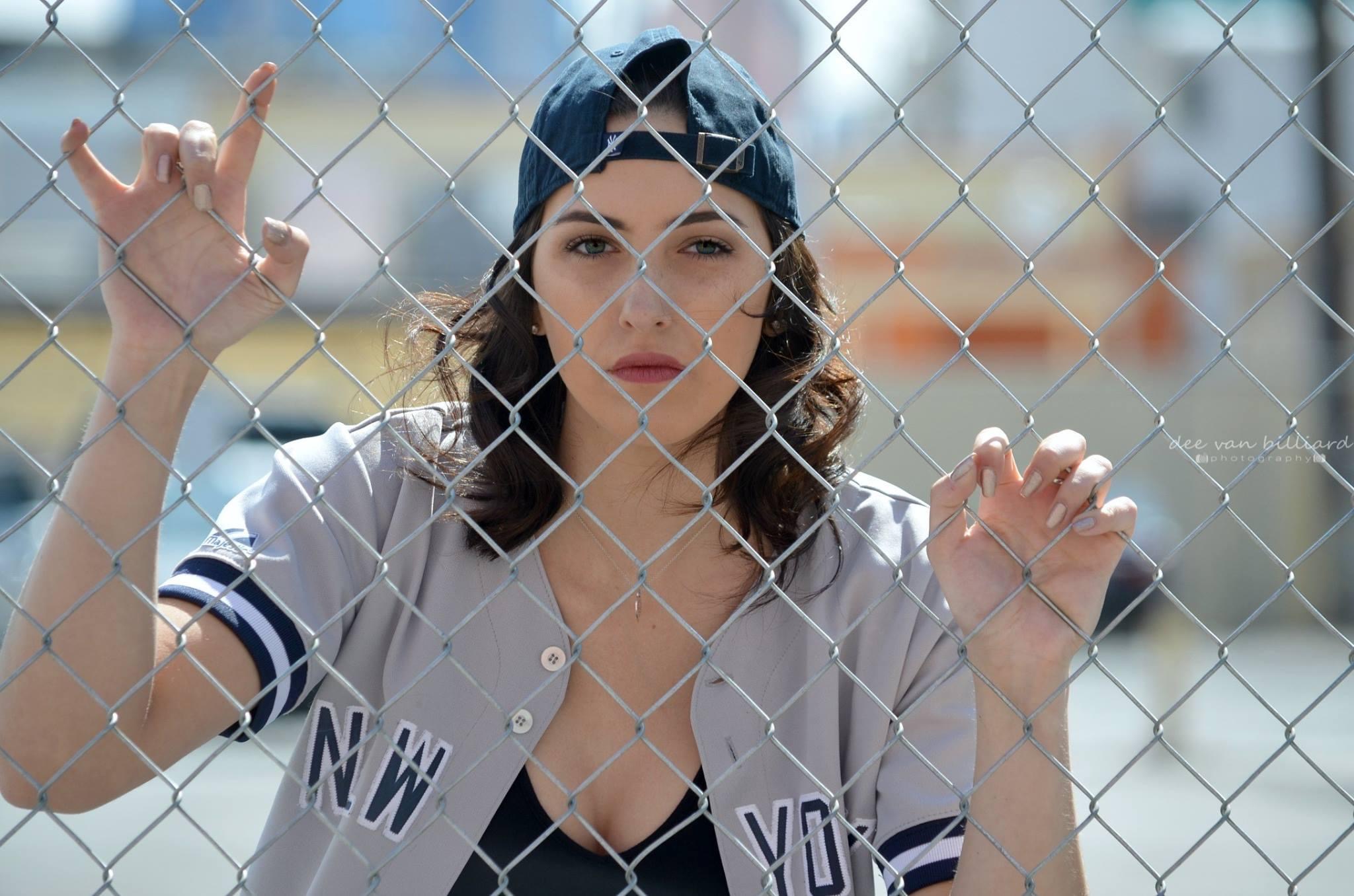A young lady poses behind the wires of a fence.