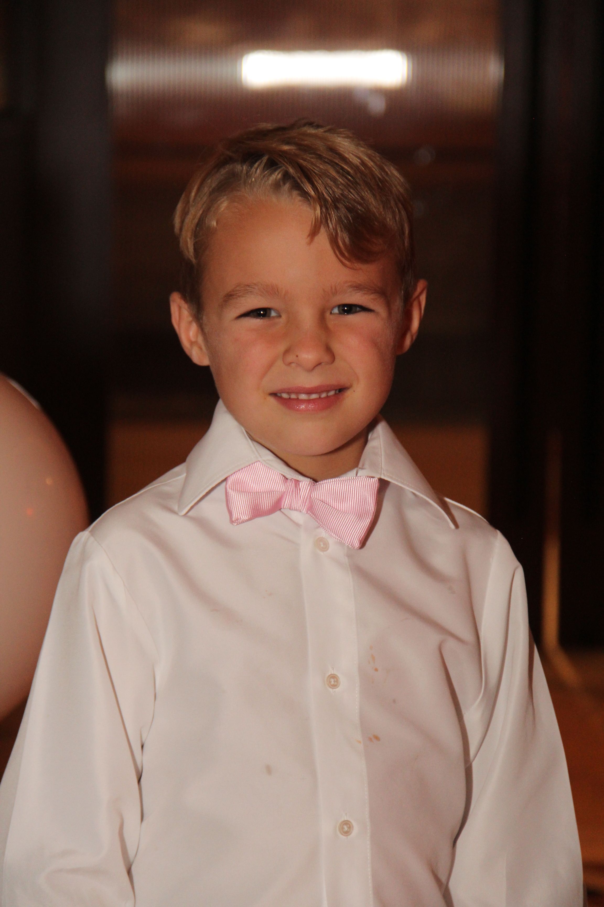 A young boy in a button up shirt smiles for the camera at a party.