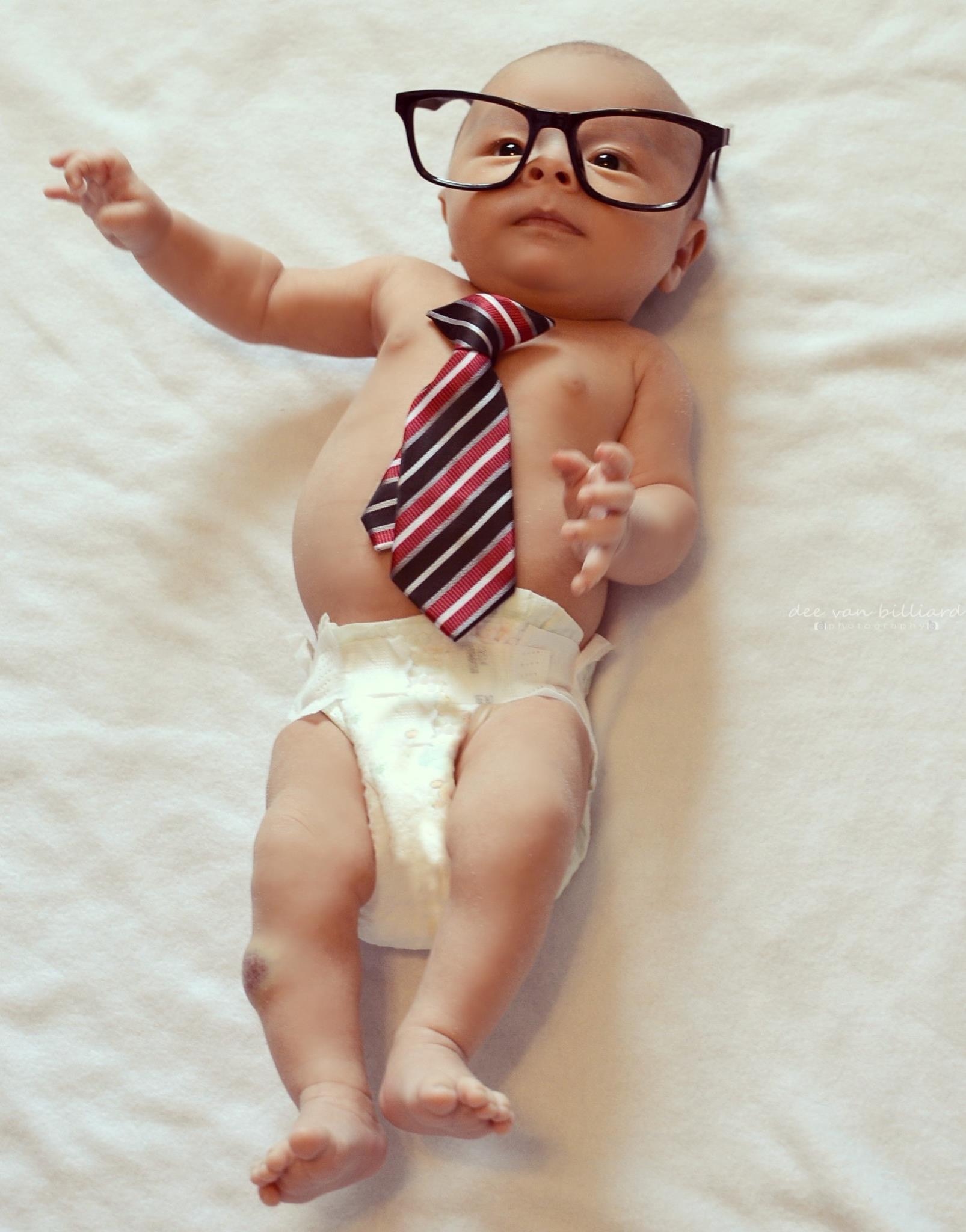A baby boy on its back wearing a large pair of glasses and a tie.