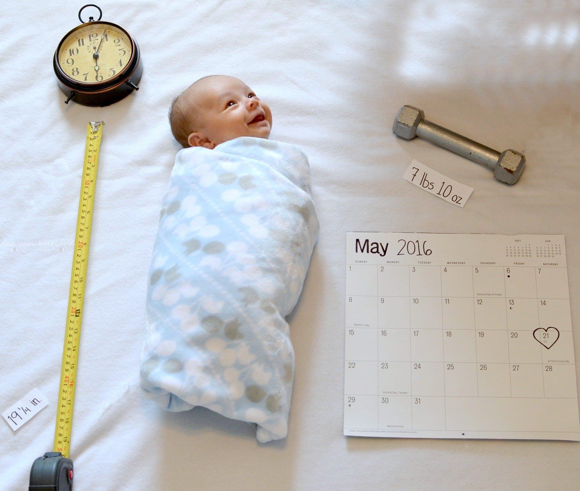 A baby wrapped in a blanket lies beside a calendar, a clock, a dumbbell, and a sign stating its weight: 7 lbs 10 oz.